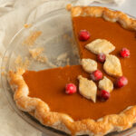 Pumpkin Pie Filling cooked in pie crust angled shot with a quarter of pie missing from pie plate.