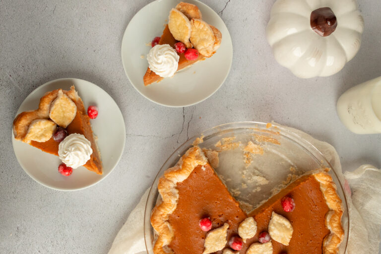 Overhead shot of pumpkin pie with 2 individual slices beside on plates.