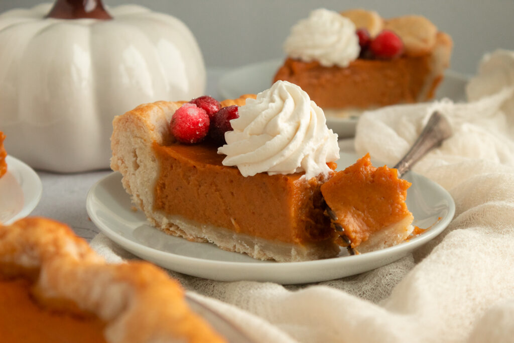 Angled shot of slice of pumpkin pie with sugared cranberries, whipped cream, and a fork.