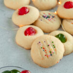 Whipped shortbread cookies with sprinkles and glaze cherries angled shot.