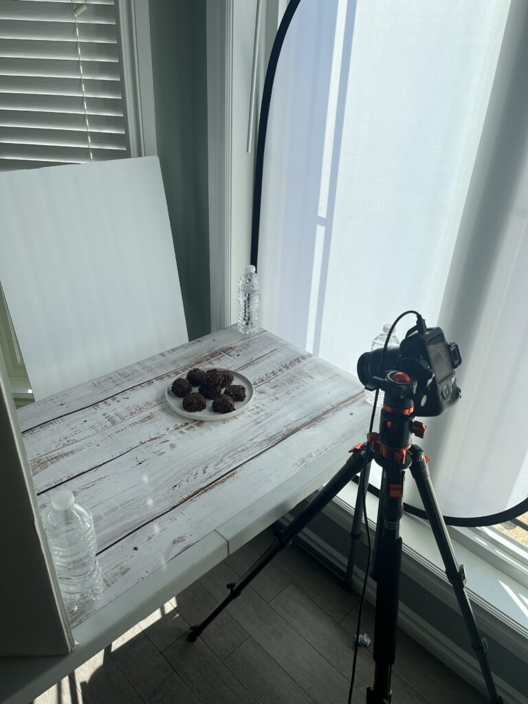 Food photography setup showing diffuser in window and plate of cookies on surface backdrop.