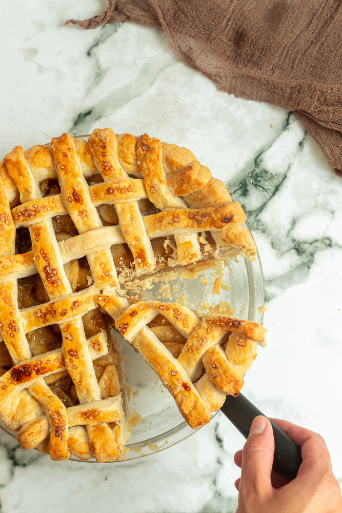 Overhead shot of Apple pie with lattice crust with a slice being served.