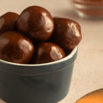 Angled shot of Chocolate Peanut butter protein balls in blue bowl with spoon of peanut butter in foreground.