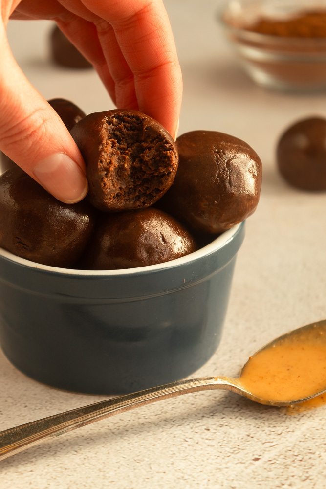 Angled shot of Chocolate Peanut butter protein balls in blue bowl with hand bite shot.