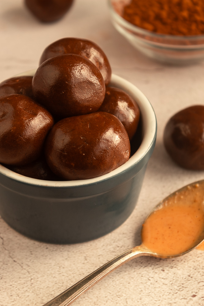 Angled shot of Chocolate Peanut butter protein balls in blue bowl with spoon of peanut butter in foreground.