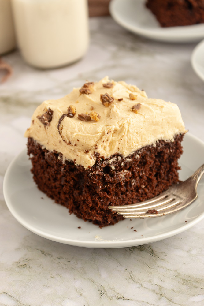 Angled shot of slice of chocolate cake with peanut butter frosting on plate with fork.