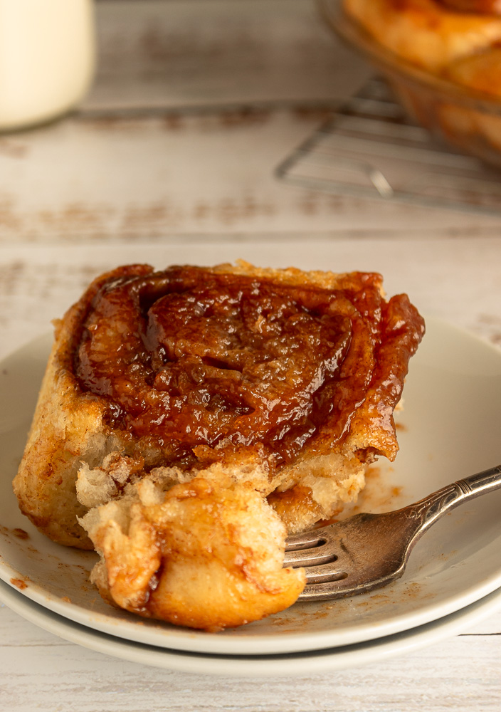 Old-fashioned cinnamon bun on plate with fork angled shot.