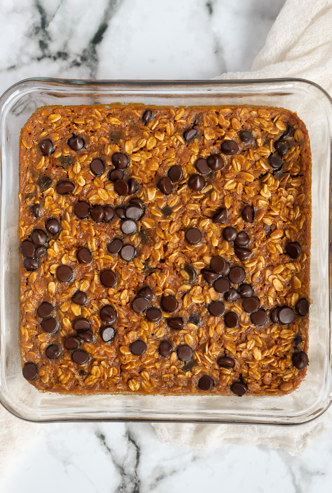 Overhead shot of Healthy chocolate chip baked oatmeal in baking pan on marble surface.