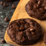 Angled shot of double chocolate fudge cookies on wooden cutting board.