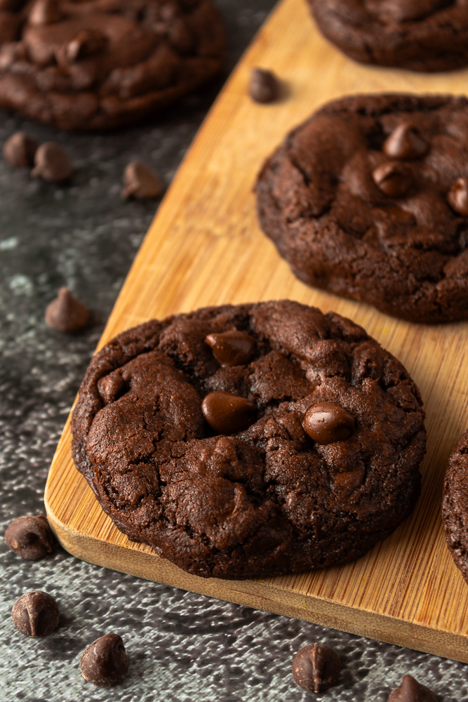 Angled shot of double chocolate fudge cookies on wooden cutting board.