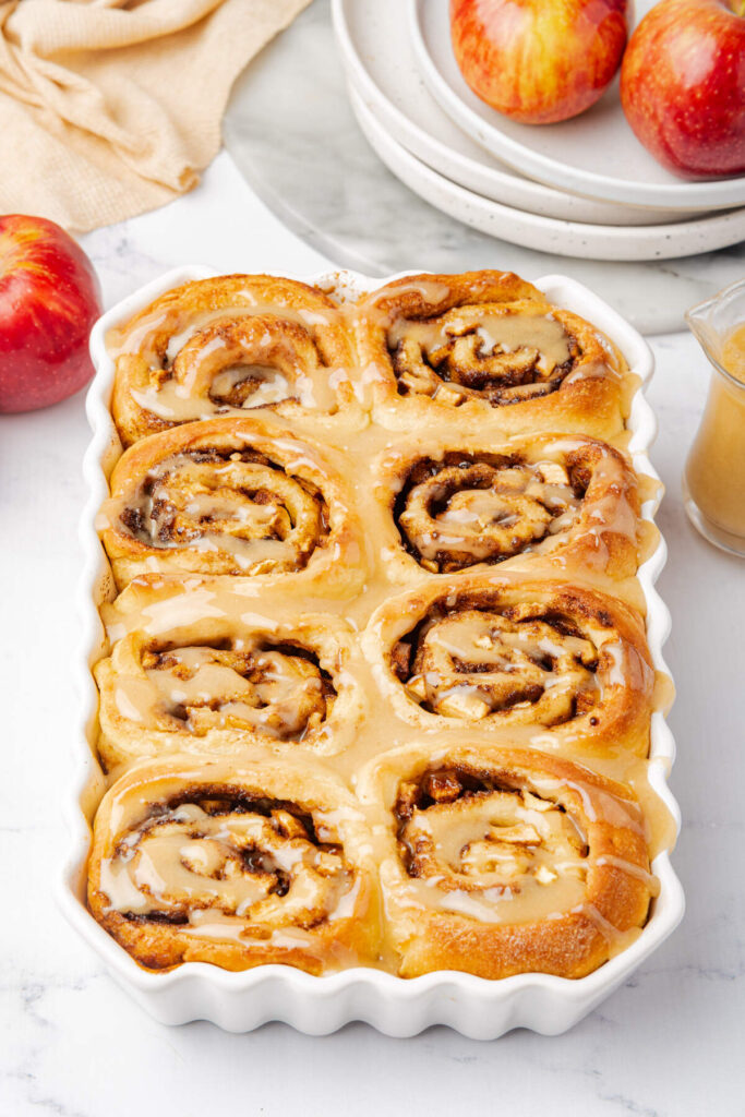 Anlged shot of apple cinnamon rolls with maple glaze in casserole dish.