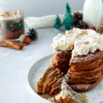 Angled shot of Easy Gingerbread pancakes stacked on plate with whipped cream, and powderede sugar and fork.