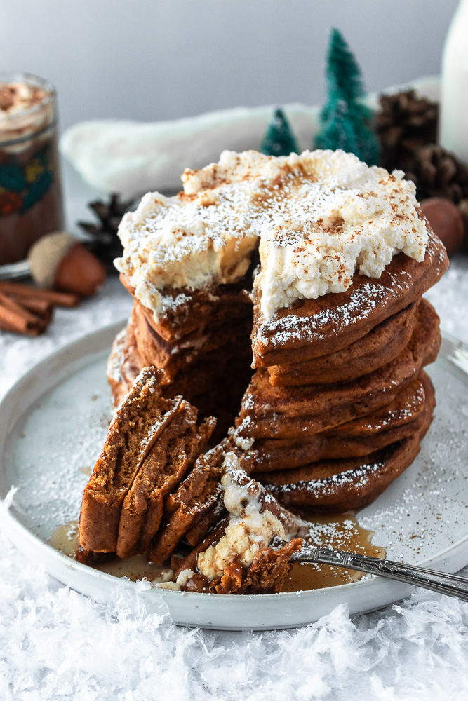 Easy Gingerbread pancakes stacked on plate with whipped cream, and powdered sugar and fork, angled shot.