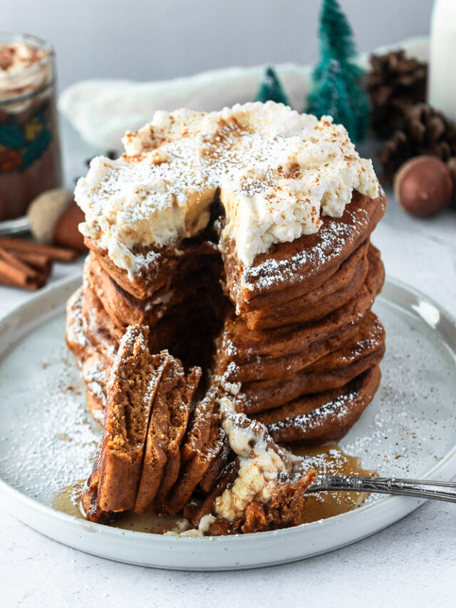 Easy Gingerbread pancakes stacked on plate with whipped cream, and powderede sugar and fork, angled shot.