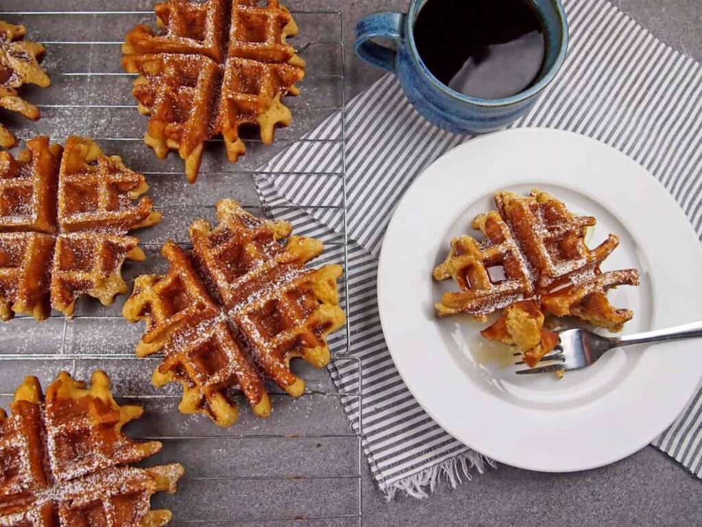 Overhead shot of spiced eggnog waffles on wire rack and plate with coffee.