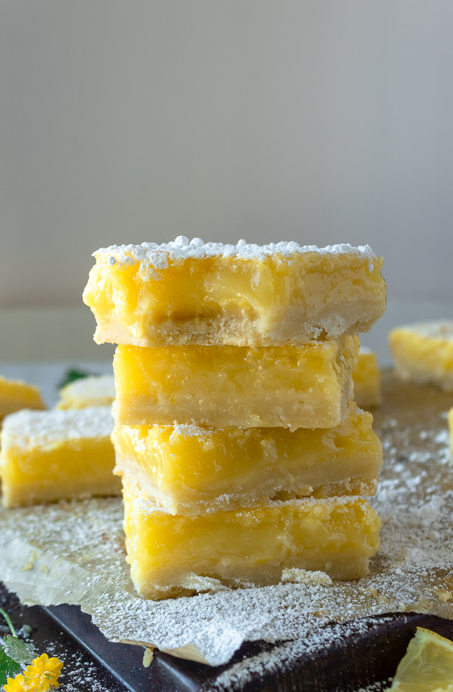 Easy Lemon bars stacked on parchment on baking pan straight on shot.