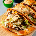 Angled shot of three smash burger tortilla wraps on wooden board.