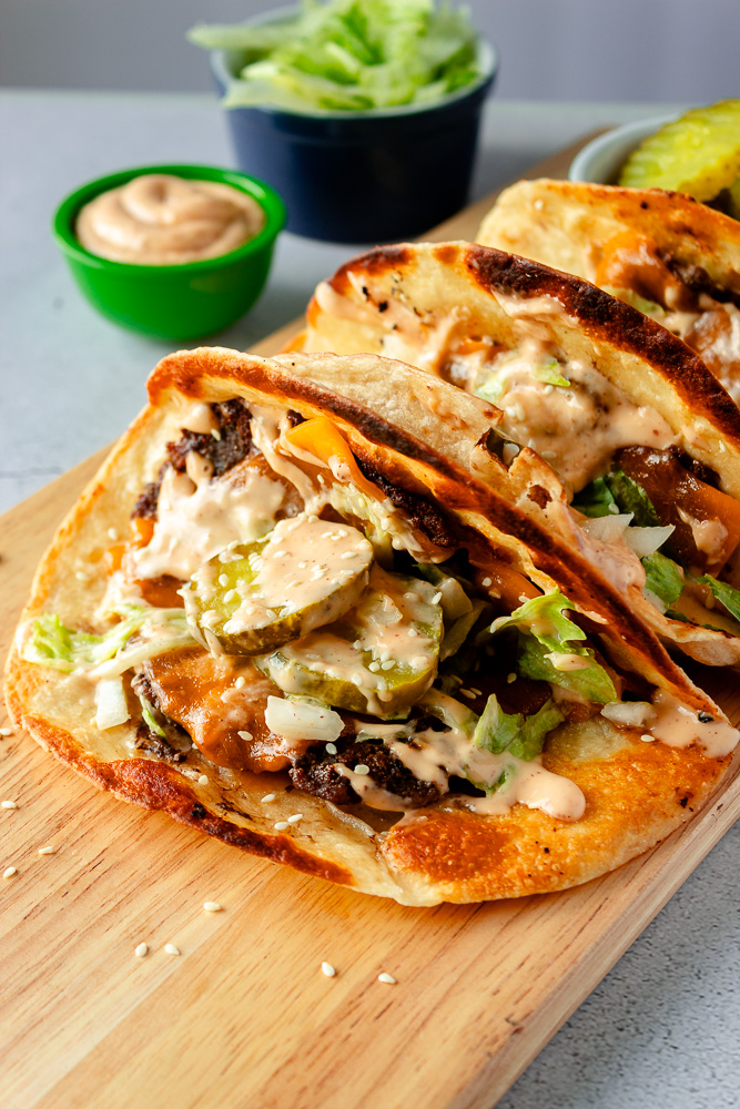 Angled shot of three smash burger tortilla wraps on wooden board.