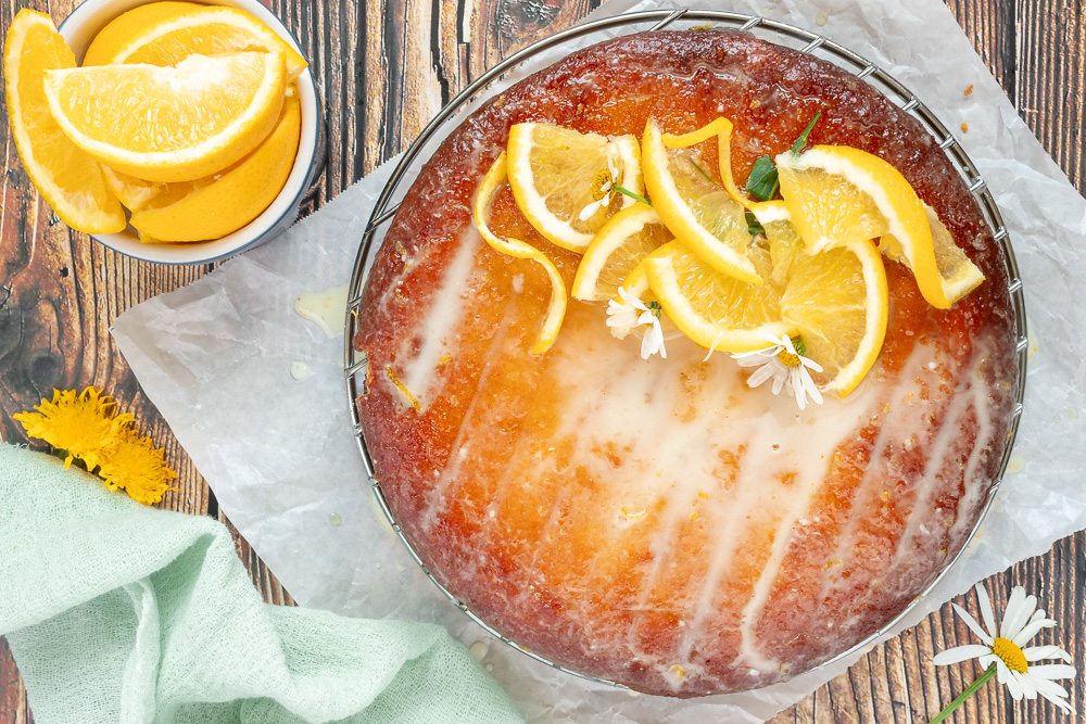Overhead shot of orange cake with glaze on parchment paper.