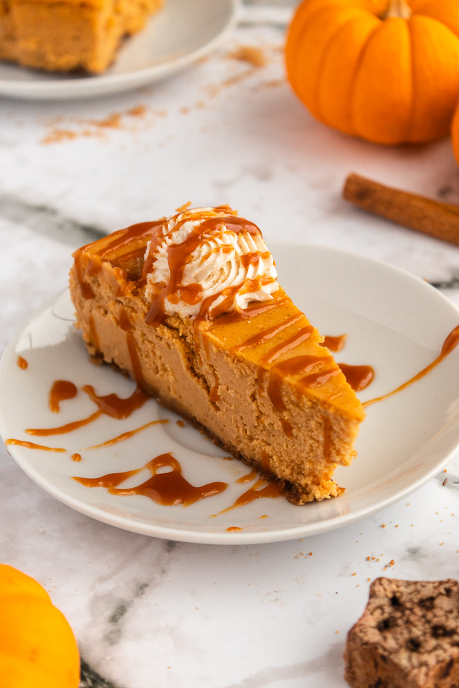 Best pumpkin cheesecake ever on a plate with whipped cream and chai caramel sauce.
